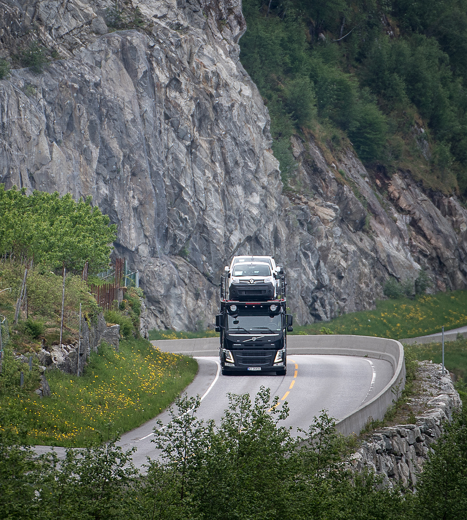 Car transport truck on road with rock wall to the right of the road